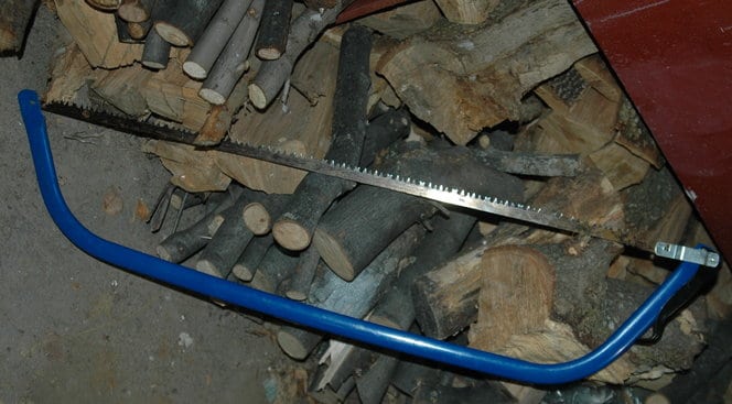 blue handle bow saw on wood pile